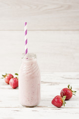 Strawberry milk in glass bottle with straw on old vintage wooden background. Fresh strawberries, light wood table.