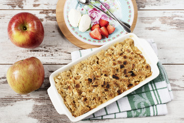 Apple crumble dessert with strawberries and vanilla cream on light rustic wooden background