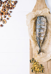 Baked fish with nuts and fish oil capsules on parchment paper and cutting board  on a white background of the old wooden boards vintage top view vertical