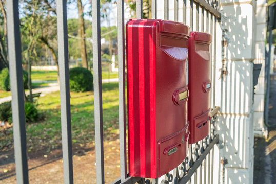 Cassette della posta rosse appese alla ringhiera di un parco pubblico