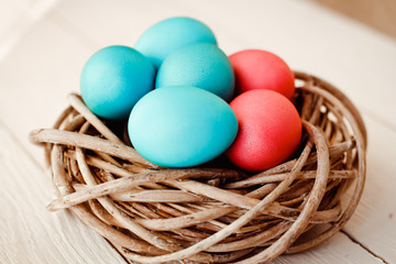 Multicolored Easter eggs in wicker basket on white wooden background