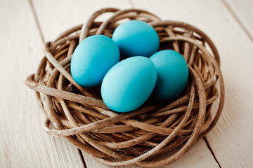 Multicolored Easter eggs in wicker basket on white wooden background