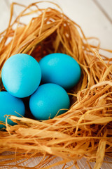 Multicolored Easter eggs in wicker basket on white wooden background
