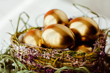 Golden easter eggs in nest on white wooden background