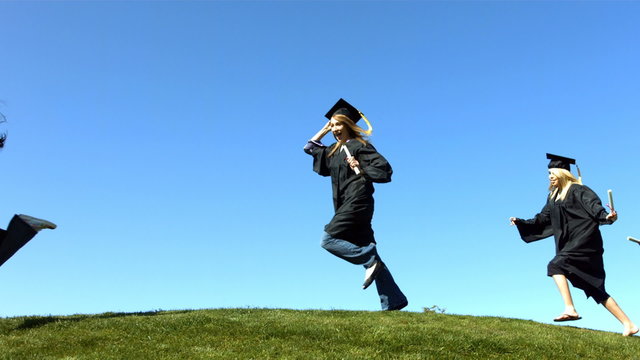 Graduates running over hill, slow motion