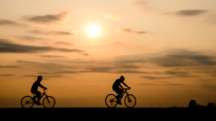 Naklejka na ściany i meble Silhouette of cyclist with friend motion on sunset background