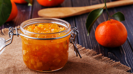 Orange (tangerine) jam in a glass jar on the table.