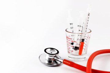 Red stethoscope with syringes in medical cup on white background.