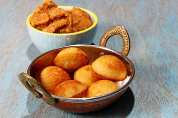 Sweet Paniyaram, a South Indian sweet made with lentils and rice batter with jaggery and coconut, selective focus. A bowl of jaggery in the background.