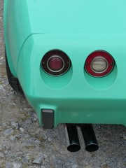 Naklejka premium Runde Rücklichter und verchromter Sportauspuff einer amerikanischen Sportwagen Ikone in Türkis auf grauem Schotter in Oerlinghausen bei Bielefeld im Teutoburger Wald in Ostwestfalen-Lippe