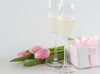 Pink fresh tulips, gift box and champagne glasses on white background