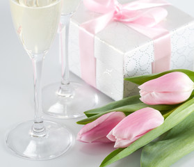 Pink fresh tulips, gift box and champagne glasses on white background