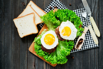 
hearty dinner , filet of beef, beefsteak with fried egg , bread - white toast, lettuce, pepper and spices on a wooden background