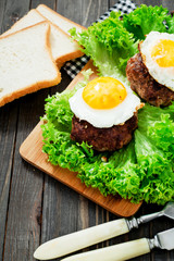 
hearty dinner , filet of beef, beefsteak with fried egg , bread - white toast, lettuce, pepper and spices on a wooden background