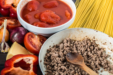 Ingredients of spaghetti bolognese arranged on wooden table.