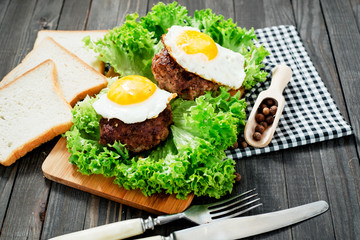 
hearty dinner , filet of beef, beefsteak with fried egg , bread - white toast, lettuce, pepper and spices on a wooden background