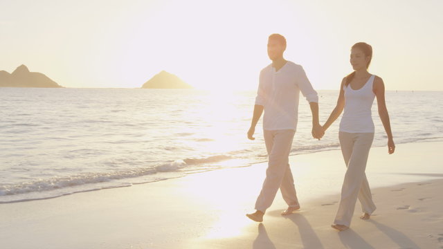 Honeymoon newlywed married young couple on beach walking in love holding hands at romantic sunrise' Multiracial woman and man relaxing on travel vacation holidays on Lanikai Beach, Oahu, Hawaii, USA  