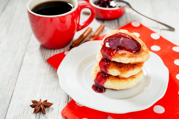 
delicious breakfast, pancakes or fritters called syrnyky from cottage cheese with strawberry or cherry jam , cinnamon and coffee on wooden background