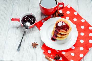 
delicious breakfast, pancakes or fritters called syrnyky from cottage cheese with strawberry or cherry jam , cinnamon and coffee on wooden background