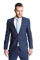 Trendy businessman standing against a white background wearing a blue suit, white shirt and a light blue tie. Staring at camera.