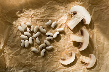 Свежие нарезанные грибы шампиньоны и белые сухие бобы на фоне пергамента вид сверху