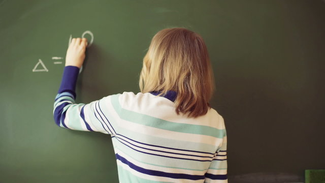 Teacher standing back and writing numbers on blackboard
