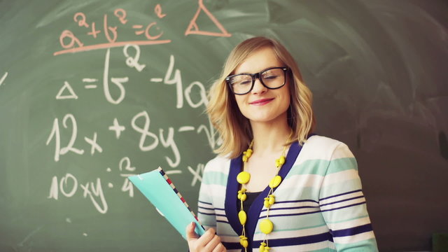 Math teacher standing in the class and smiling to the camera

