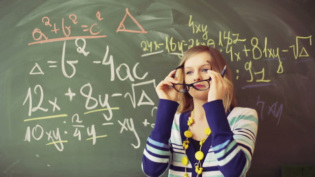 Thoughtful teacher standing next to the blackboard full of numbers
