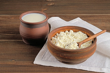 Cottage cheese  and milk. Cottage cheese in a wooden bowl and milk in a ceramic pot on a brown wooden background.