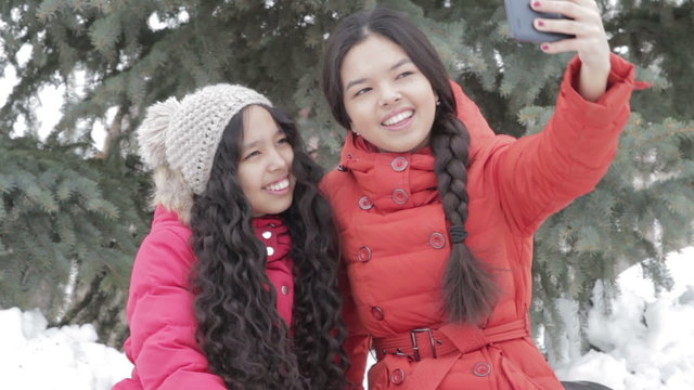 Smiling two girl taking a selfie with smartphone outdoors in warm clothes