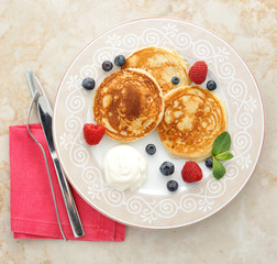pancakes with sour cream on the plate with raspberries and blueb
