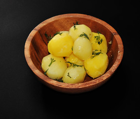 Boiled potato in wooden bowl with dill and butter.