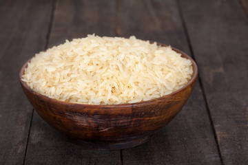 Raw plain rice in wooden bowl on rustic table
