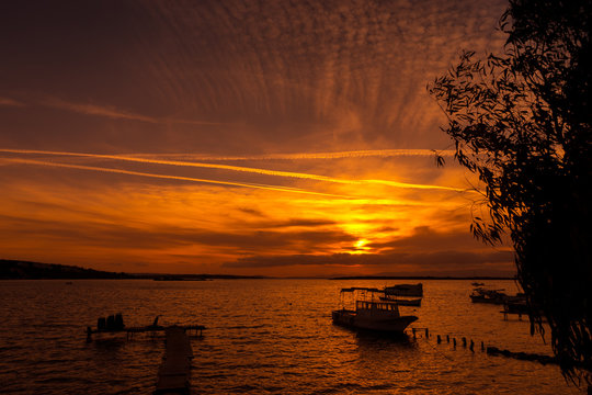 Sunset on Cesme beach with sailing boats through tree leafs