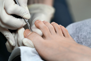 Close up pedicure process. Master working with cuticle remuver