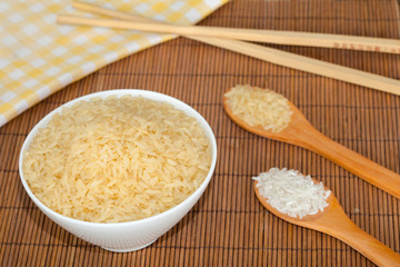Uncooked rice with spoons and sticks, bamboo background