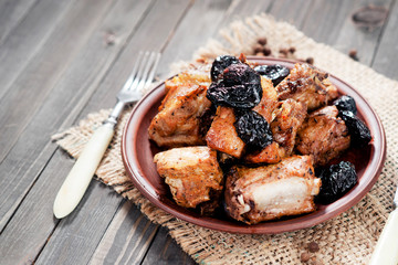 Baked or fried meat , pork ribs with prunes , spices and pepper on a dark wooden background