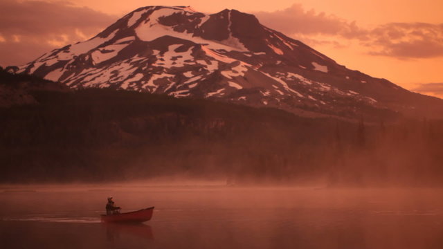 Man rows canoe at sunrise