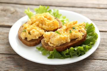 Scrambled eggs with bread and vegetables on a grey wooden table