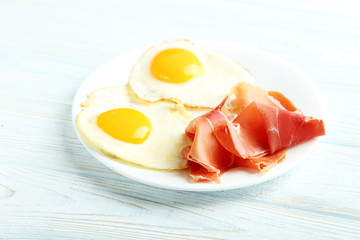 Fried eggs with bacon on plate on blue wooden table