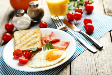Fototapeta na wymiar Fried eggs with bacon and toasts on plate on grey wooden table