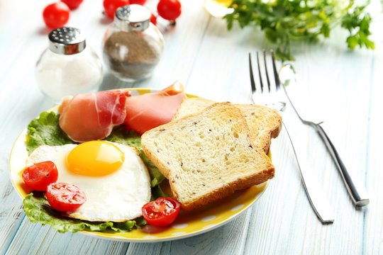 Fried eggs with bacon and toasts on plate on blue wooden table