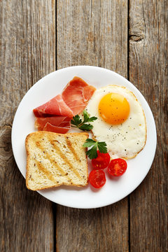 Fried eggs with bacon and toasts on plate on grey wooden table