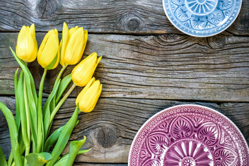 Fresh yellow tulip flowers on wooden table with ancient plates. Top view with copy space.  over wooden background.