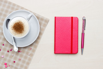 Red notebook with pen and coffee on wooden