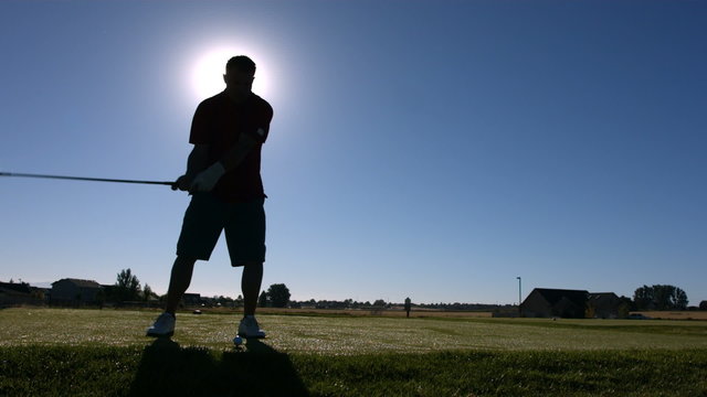 Silhouette of golfer teeing off, slow motion