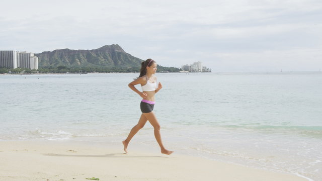 Young woman running on sea shore. Determined female is in sportswear. Runner is exercising on sunny day. Idyllic view of sea and mountain against sky.
