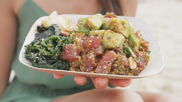 Midsection of woman holding poke salad plate. Closeup of female with traditional Hawaii dish consisting of raw marinated ahi yellowfin tuna fish at beach. Tourist is representing her healthy lifestyle