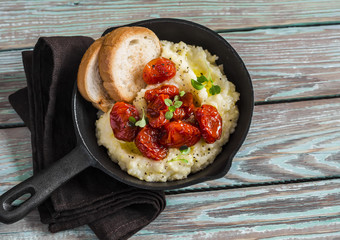 Roasted tomatoes with goat cheese polenta in vintage pan on a dark wooden background. Healthy vegetarian food