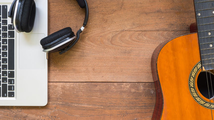 Top view workspace with laptop,headphone and acoustic guitar on wooden table.